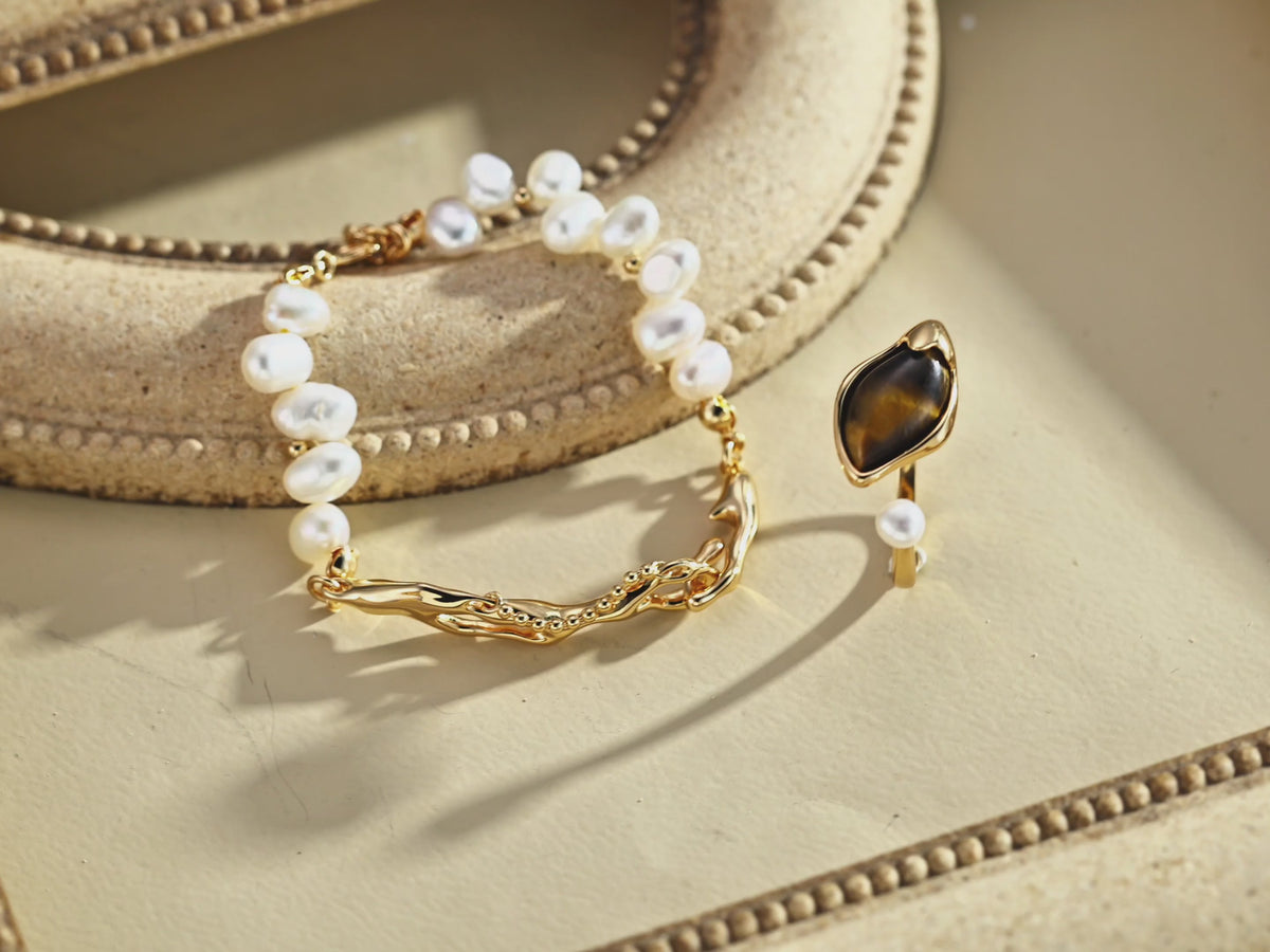 Tiger’s eye and freshwater pearl open ring in Vintage Gold beside a pearl bracelet with sculptural gold-tone links.