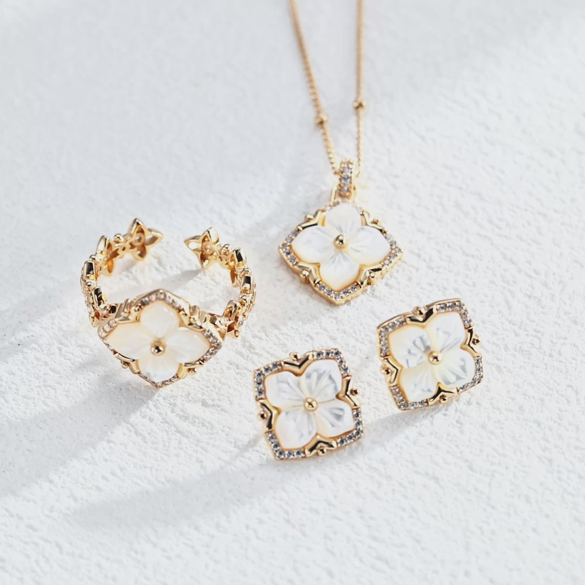 A video of a jewelry set of 18K White Gold Plated S925 Silver floral stud earrings with white mother-of-pearl flower centers and cubic zirconia halos, matching necklace and open ring